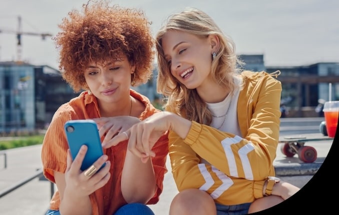 Two women sitting outside looking at mobile phone.