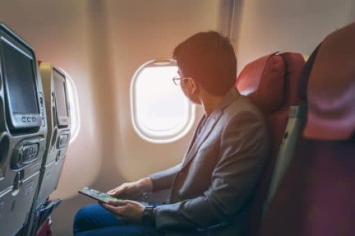 Man holding a magazine looks out airplane window.