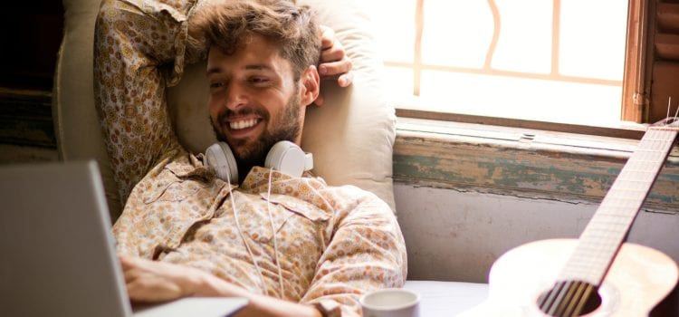 Man with headphones around his neck smiling at his computer.